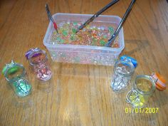 a plastic container filled with lots of different colored beads next to two black tongs