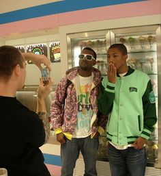 three young men standing in front of a display case looking at their cell phones and taking pictures