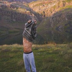 a man standing on top of a lush green hillside next to mountains with his hands in the air