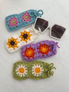 three crocheted sun glasses cases with flowers on them and one pair of sunglasses