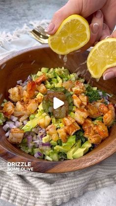 someone is squeezing lemons into a salad in a wooden bowl with shrimp and lettuce