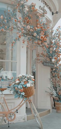 a bicycle parked in front of a store with flowers on the back and branches hanging from it