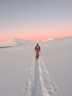 a man riding skis down a snow covered slope at sunset or dawn in the mountains