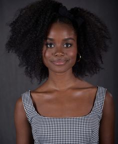 a woman with an afro standing in front of a gray background wearing a black and white checkered top