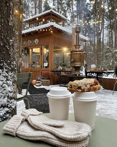 two cups of coffee sitting on top of a table next to a snow covered forest