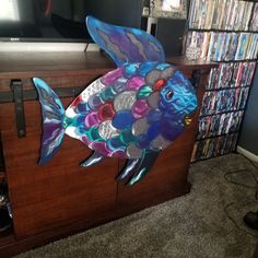 a fish made out of cds on top of a wooden entertainment stand in front of a television
