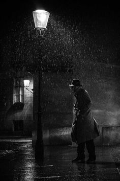 black and white photograph of two people standing in the rain under a street light at night