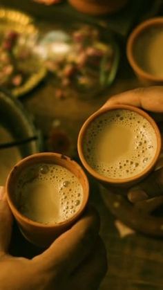 two hands holding three mugs filled with liquid