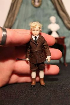 a hand holding a small doll in front of a miniature man's suit and tie