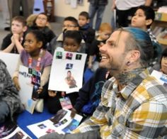 a man sitting in front of a group of children with pictures on the wall behind him