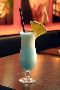 a blue drink with a pineapple on the rim sits on a table in a restaurant