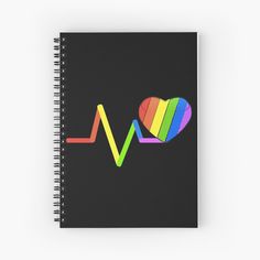 a spiral notebook with a rainbow heart and heartbeat on the front, against a black background