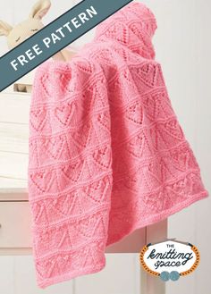 a pink knitted blanket sitting on top of a wooden table next to a white dresser