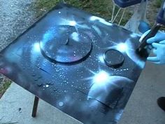 a person in blue gloves is using a tool to paint a solar system on a table