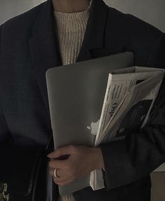 a woman in a business suit holding an apple laptop and folders with both hands