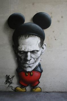 a wall with a painting of mickey mouse on it's face and ears, in front of a cement wall