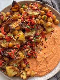 a white plate topped with potatoes, tomatoes and garnished in red pepper sauce