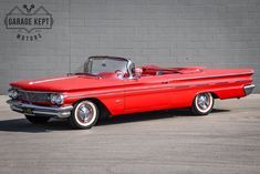 an old red convertible car parked in front of a brick wall with garage kept written on it