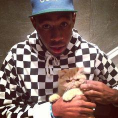 a man holding a cat in his arms while wearing a hat and checkered shirt