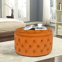 an orange tufted ottoman sits in front of a bed