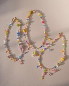 three bracelets with beads and charms hanging from the side on a white table top
