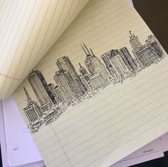 a piece of paper with a drawing of a city on it next to a notebook