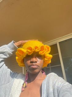 a woman wearing a yellow crochet hat with flowers on it's head