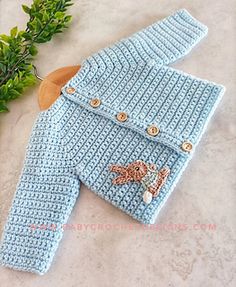 a crocheted blue sweater with buttons on it next to a wooden spoon and plant