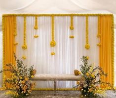 a decorated stage with yellow drapes and flowers on the side, along with two benches