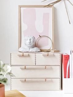 a white dresser topped with drawers next to a potted plant and a framed art piece