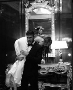 a man in a tuxedo is hugging a woman's head while standing next to a mirror