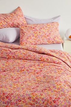 a bed with pink and yellow floral comforter set on it's headboard