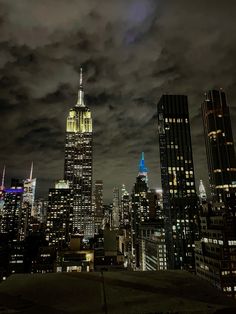 the city skyline is lit up at night, with clouds in the sky and lights on