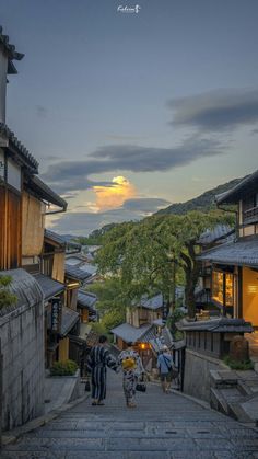 two people walking down an alley way with buildings and mountains in the background at dusk