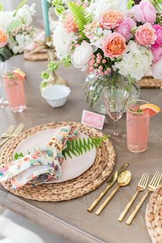 the table is set with pink and white flowers in vases, napkins, and goldware