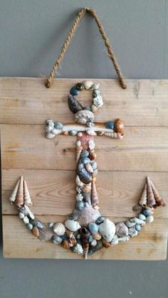 an anchor made out of seashells and rope hangs on a wooden sign with string