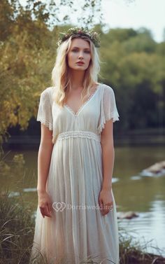 a woman wearing a white dress standing in front of a body of water and trees