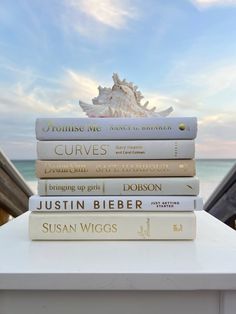 a stack of books sitting on top of a white table in front of the ocean