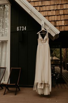 a wedding dress hanging on a hanger in front of a black building with a brown shingled roof