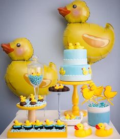 a table topped with yellow rubber ducks next to cake and balloons in the shape of ducklings