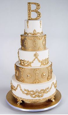 a white and gold wedding cake with the letter b on top