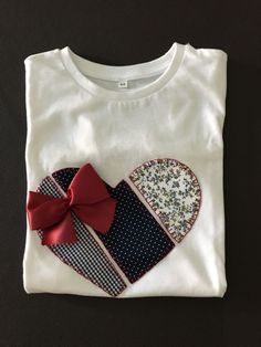 a white t - shirt with a red bow and patchwork heart on the front