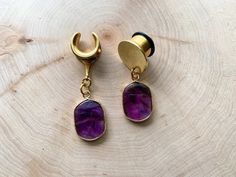 a pair of gold earrings with amethyst purple stones hanging from them on a piece of wood