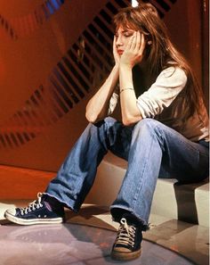 a young man sitting on top of a white bench next to a red wall with his hands in his face