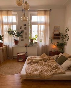 an unmade bed in front of two windows with plants on the window sill