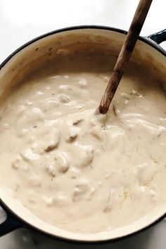 a pot filled with white sauce on top of a stove next to a wooden spoon