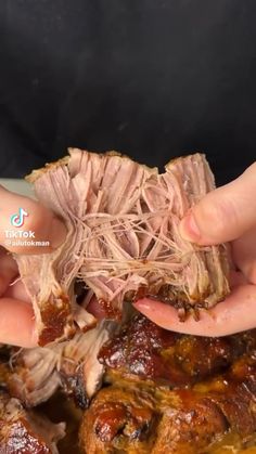 two hands holding some meat on top of a white plate in front of another person