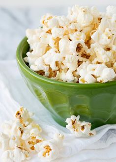 a green bowl filled with popcorn on top of a white cloth