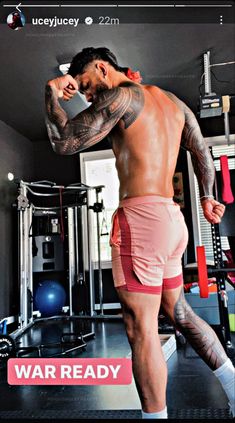 a man with tattoos on his arm and leg standing in front of a gym machine