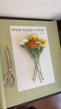 a pair of scissors sitting on top of a piece of paper next to some flowers